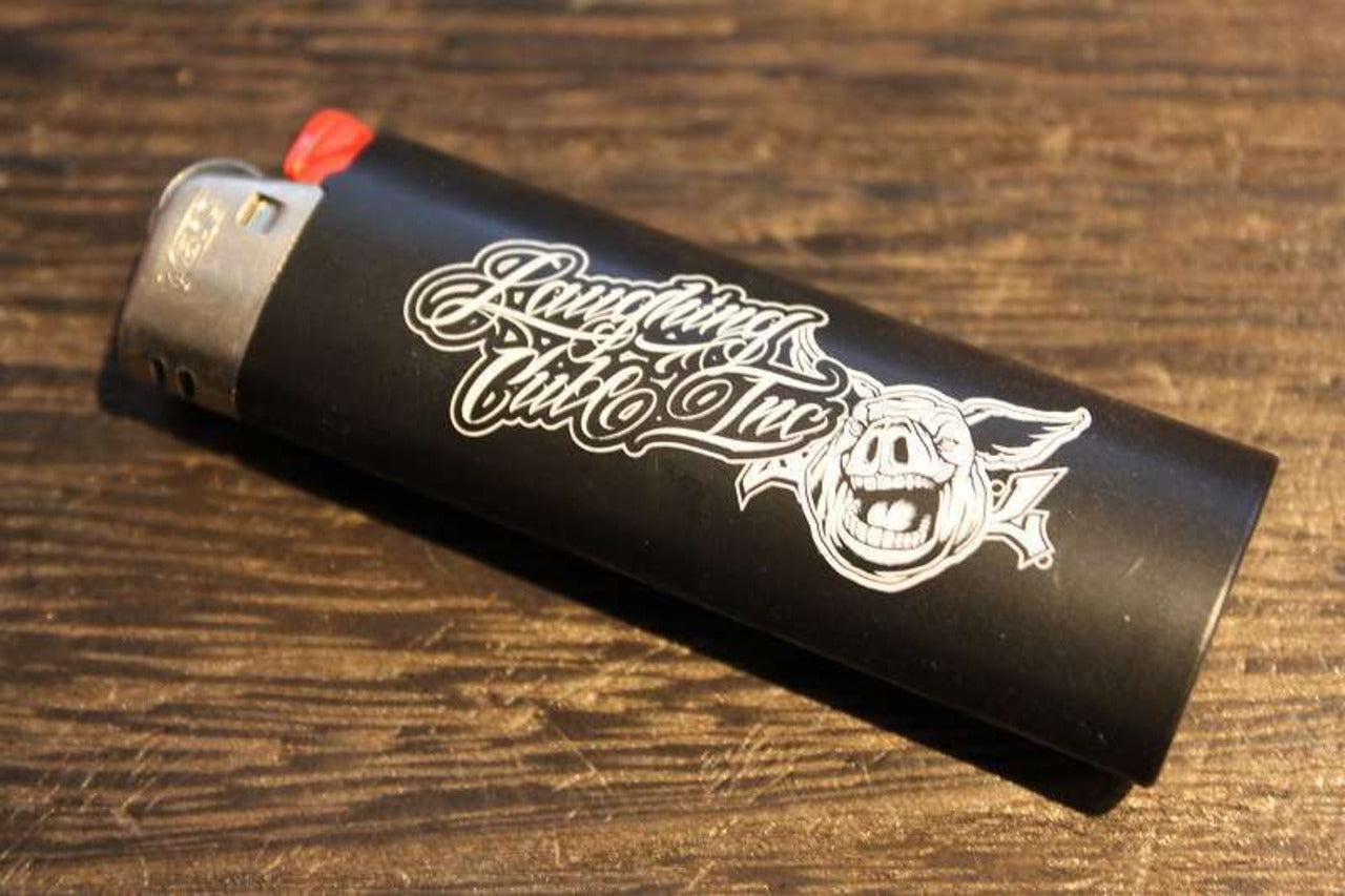 Laughing Club Incのロゴとブタのイラストがプリントされた黒いライターの画像。