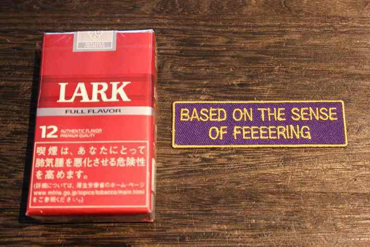 紫地に黄色い英字で『BASED ON THE SENSE OF FEEEERING』と刺繍された長方形ワッペン。英語メッセージ入り刺繍パッチ