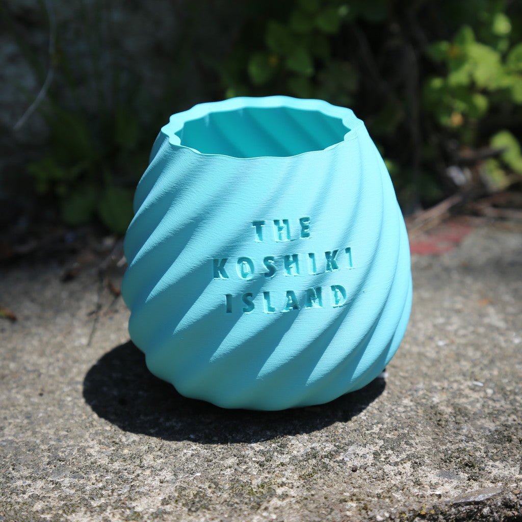 THE KOSHIKI ISLANDの文字が彫られた、水色のマットな質感の多角形カップ。ひねりのある立体形状が特徴で、09969。jpによる甑島オリジナルグッズの画像9