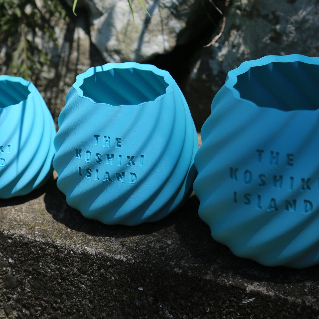 THE KOSHIKI ISLANDの文字が彫られた、水色のマットな質感の多角形カップ。ひねりのある立体形状が特徴で、09969。jpによる甑島オリジナルグッズの画像8
