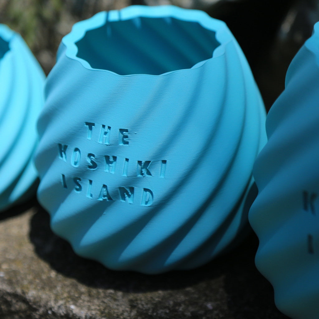THE KOSHIKI ISLANDの文字が彫られた、水色のマットな質感の多角形カップ。ひねりのある立体形状が特徴で、09969。jpによる甑島オリジナルグッズの画像6