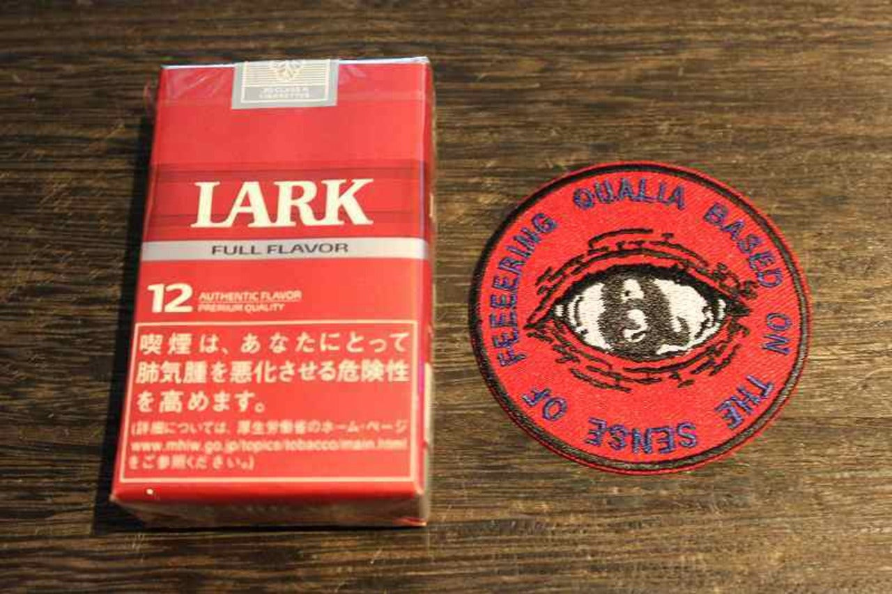 赤い背景に目のデザインと英語テキストが刺繍された丸型ワッペン。『QUALIA BASED ON THE SENSE OF FEELERING』の文字が円形に配置され、中央にはリアルな瞳の刺繍。個性的でインパクトのある刺繍ロゴパッチの画像2