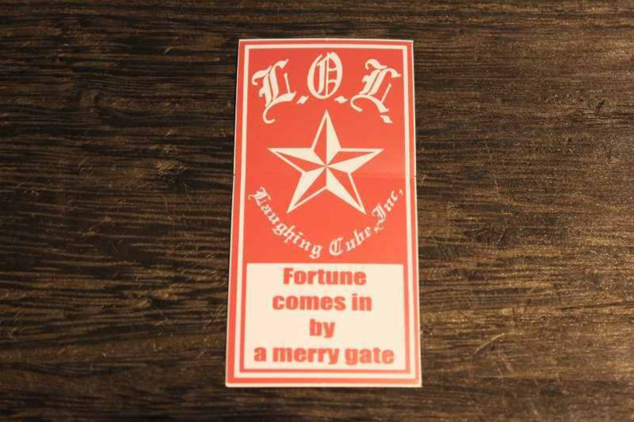 L.O.L.のロゴと星マーク、「Fortune comes in by a merry gate」の英語メッセージがデザインされた赤地の縦長ステッカー