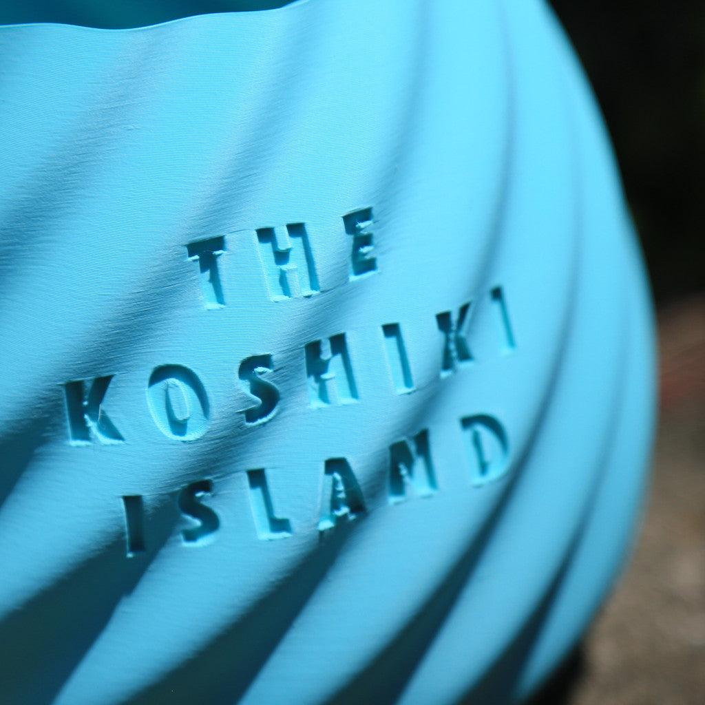 THE KOSHIKI ISLANDの文字が彫られた、水色のマットな質感の多角形カップ。ひねりのある立体形状が特徴で、09969。jpによる甑島オリジナルグッズの画像7