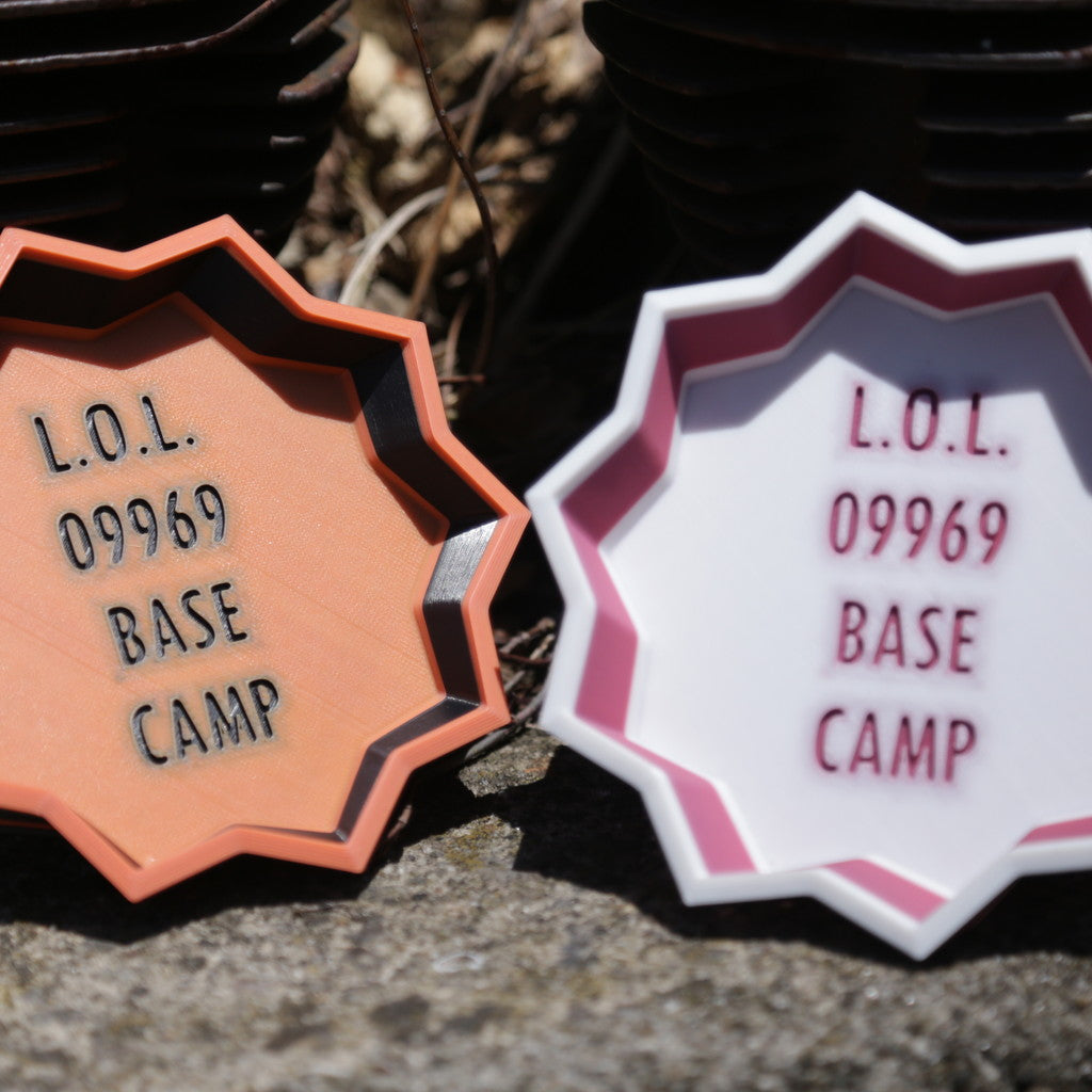 「L.O.L 09969 BASE CAMP」の文字が入った八角形のプレートキーホルダー。ホワイトとテラコッタカラーの2色展開で、甑島の観光拠点・09969ベースキャンプのオリジナルグッズ