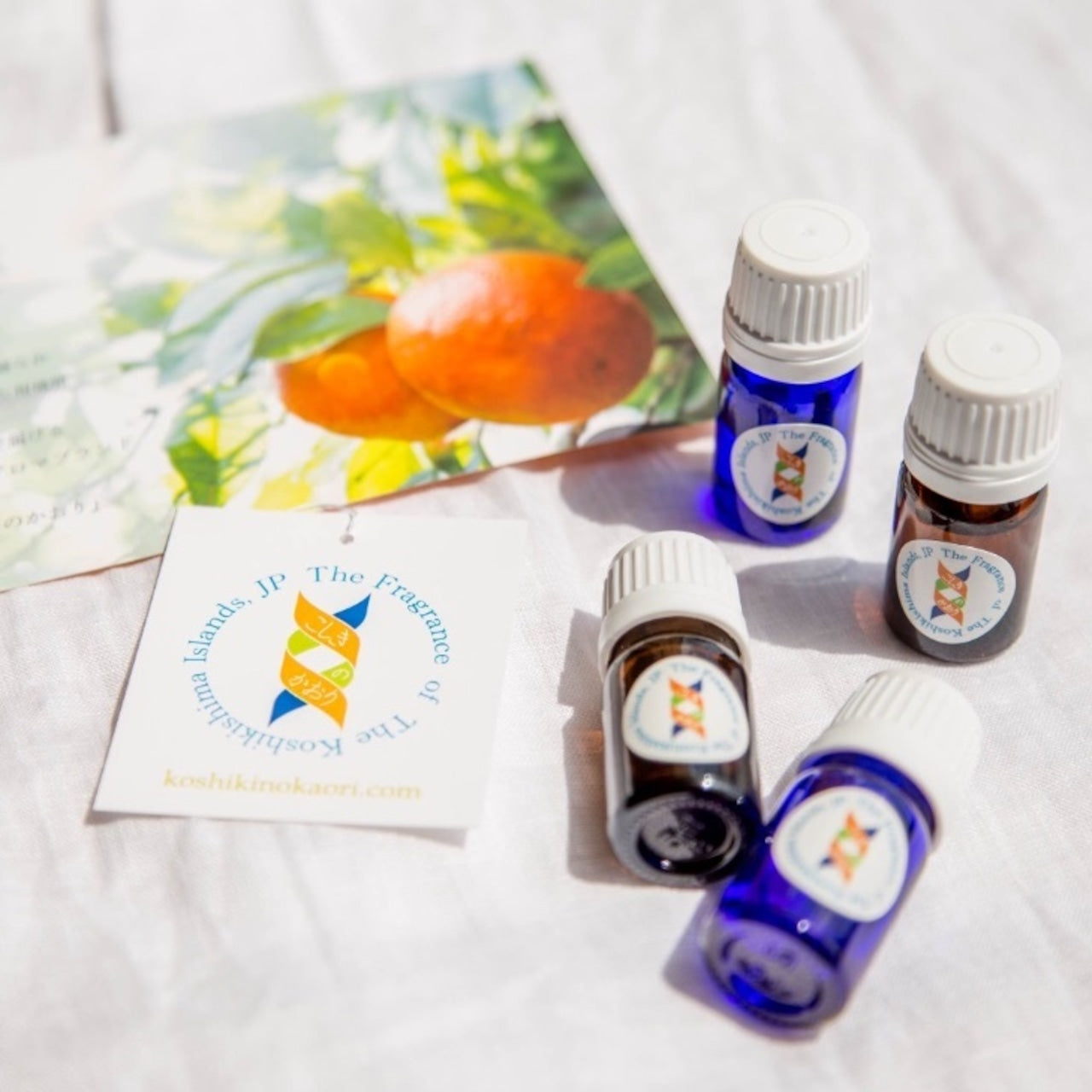 甑島産の柑橘を使用した精油「The Fragrance of Koshikijima」のアロマオイル。自然由来の香りとともに、みかんの写真やブランドタグが並ぶ商品イメージ。甑島、アロマ、柑橘、クラフト、特産品、精油、ナチュラルアイテムに関心のある層に最適