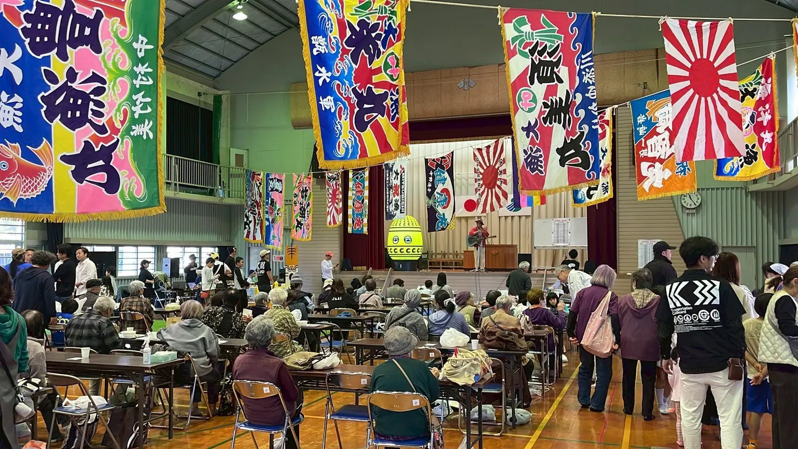 大漁旗が飾られた体育館に集まる人々